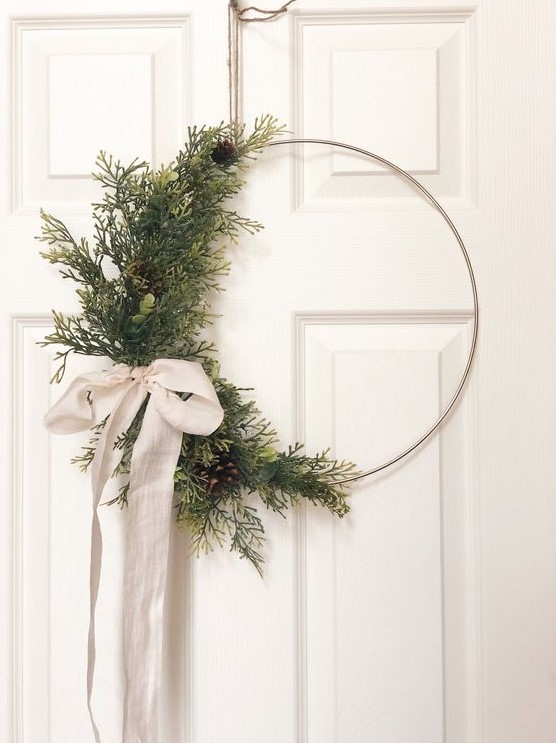 a modern Christmas wreath with evergreens and pinecones on one side and a neutral ribbon bow is a lovely decor idea