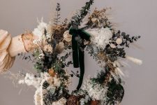 a modern boho Christmas wreath with dried grasses, leaves, pinecones and faux berries and a green bow on top