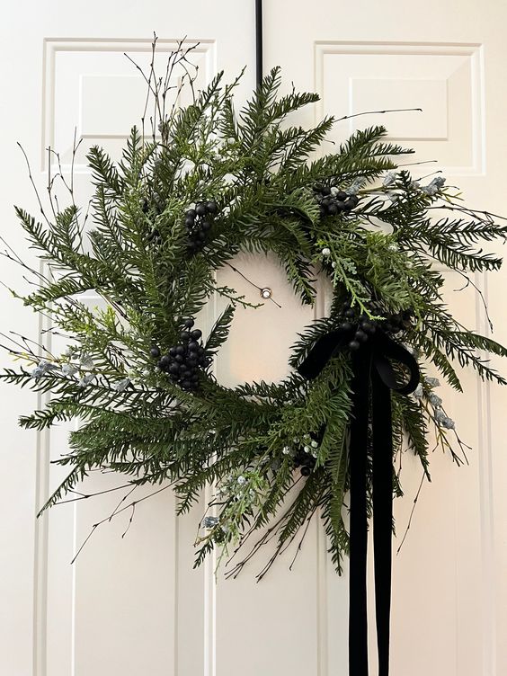 a modern dimensional Christmas wreath of evergreens, twigs, berries and a black bow for a modern or Scandinavian space