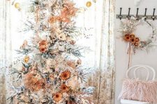 a pretty boho natural Christmas tree decorated with lights, dried and fabric blooms, blooming branches and berries and some burlap at the base