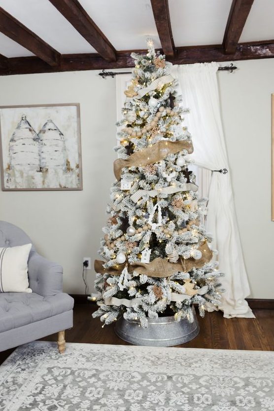a rustic flocked Christmas tree with burlap ribbon, lights, white and metallic ornaments placed into a metal surround