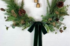 an elegant modern Christmas wreath with evergreens, greenery, branches, pinecones, berries, vintage bells and a dark green bow
