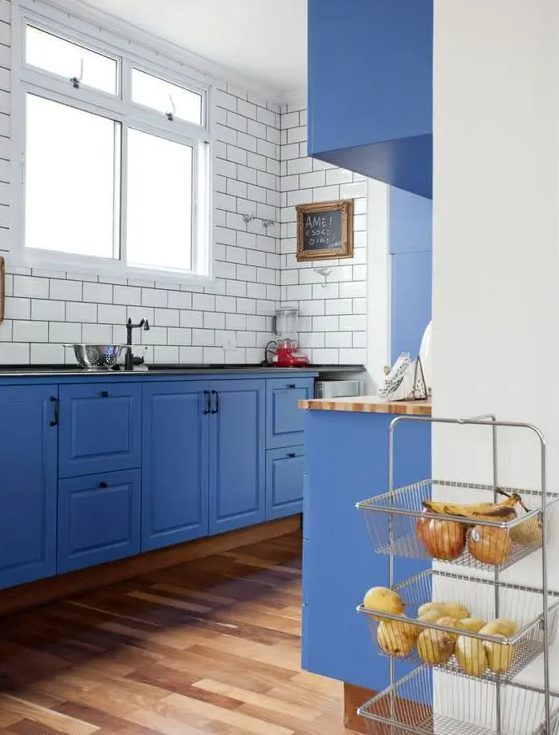 a bold blue kitchen with white subway tiles and black grout to stand out plus butcherblock and black countertops