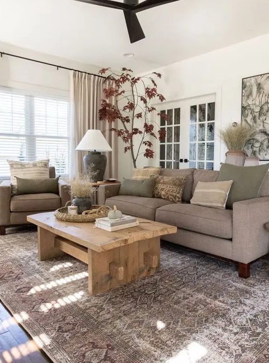 a modern earthy living room with grey seating furniture, a low wooden table, a printed rug, earthy pillows and potted plants