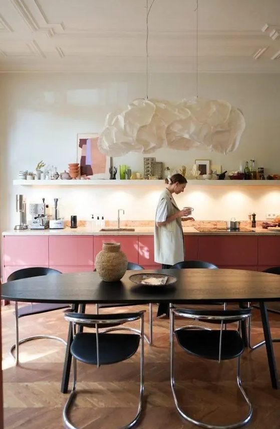 A bold pink kitchen with lower cabinets, a terrazzo countertop, a long shelf with decor and some built in lights