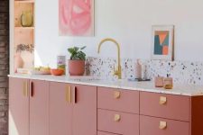 06 a modern and stylish pink kitchen with a terrazzo backsplash and countertops, gold hardware and a faucet, a niche for storage