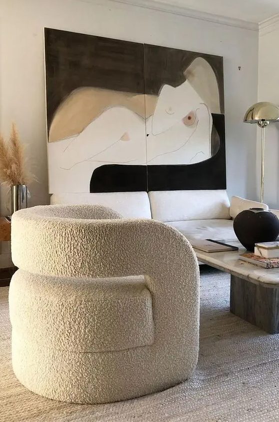 a refined living room with a creamy sofa, a coffee table, a curved chair, a statement artwork and pampas grass