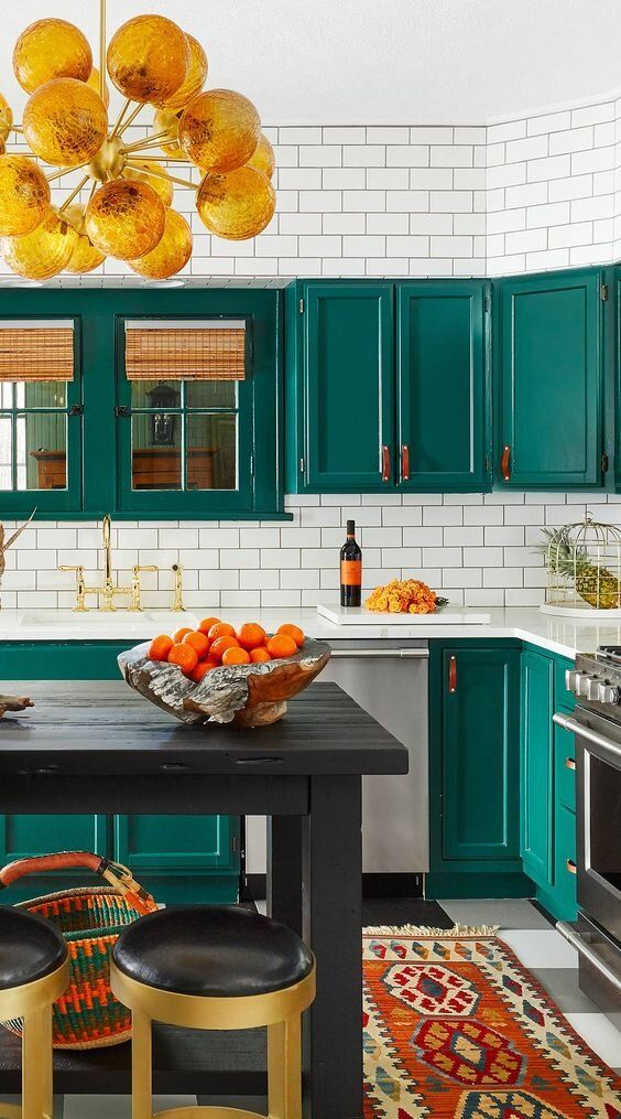an emerald kitchen with shaker cabinets, white subway tiles, a gold buble chandelier and a black kitchen table and island in one