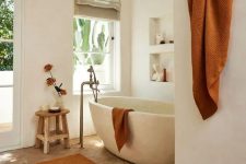 13 a beautiful earthy bathroom with white plaster walls, a parquet flooring, a stone bathtub, niches with decor and rust textiles