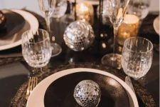 15 a black and silver NYE tablescape with black printed placemats, black and white plates, black candles and silver disco balls