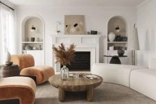 16 a modern earthy living room with a fireplace, rust-colored chairs, a neutral curved sofa, a low coffee table and niches with decor