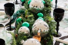 17 a bright NYE party table with evergreens, silver disco balls, green ornaments and black glasses plus green napkins