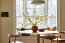 19 an earthy dining room with a bay window with a window seat, a round table and mid-century modern chairs, a pendant lamp