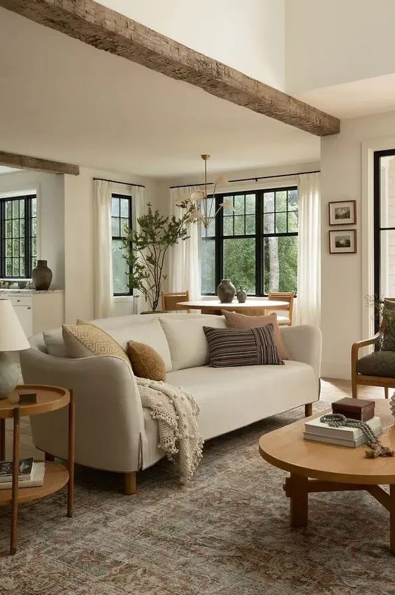 an earthy living room with a neutral sofa, a green chair, a low coffee table and a side one, a rough wooden beam