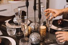 22 a NYE tablescape with black as a basic color, black candles and plates, disco balls, gold cutlery and gold-rimmed glasses