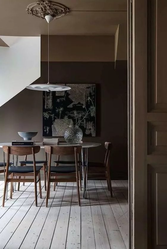 A moody all taupe dining space with a neutral floor, an oval hairpin leg table, black chairs and a pendant lamp