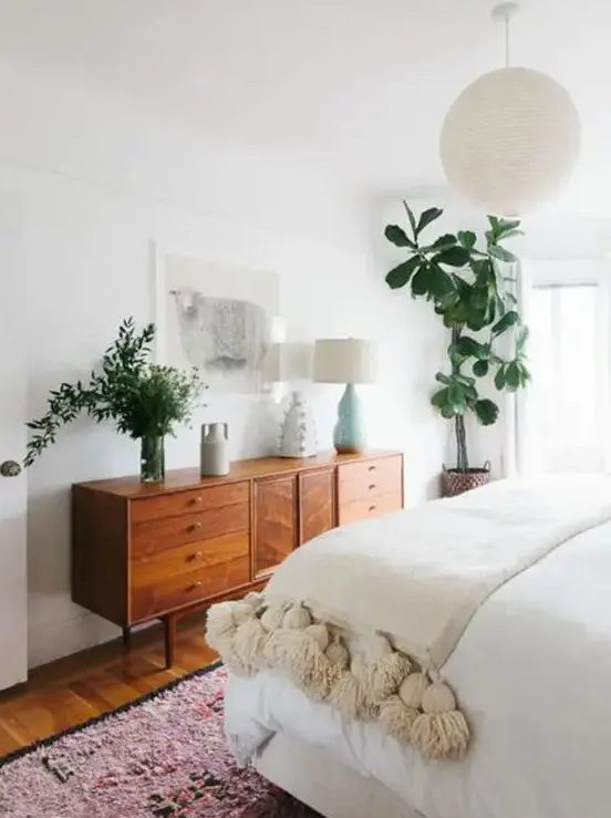 a mid-century modern stained dresser is used both for storage and for styling the space, it displays lamps and greenery
