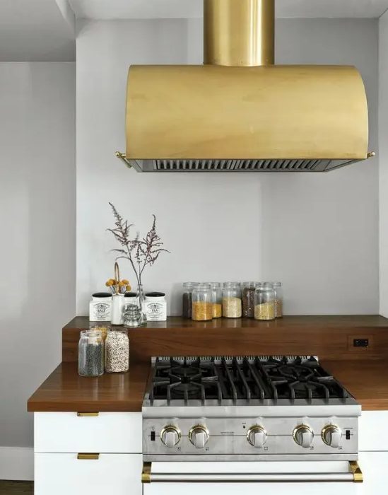 a sleek white kitchen with dark stained countertops. a gold statement hood that adds chic and elegance to the space