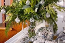 26 NYE decor with evergreens with silver disco balls and some more disco balls on the table is amazing and shiny
