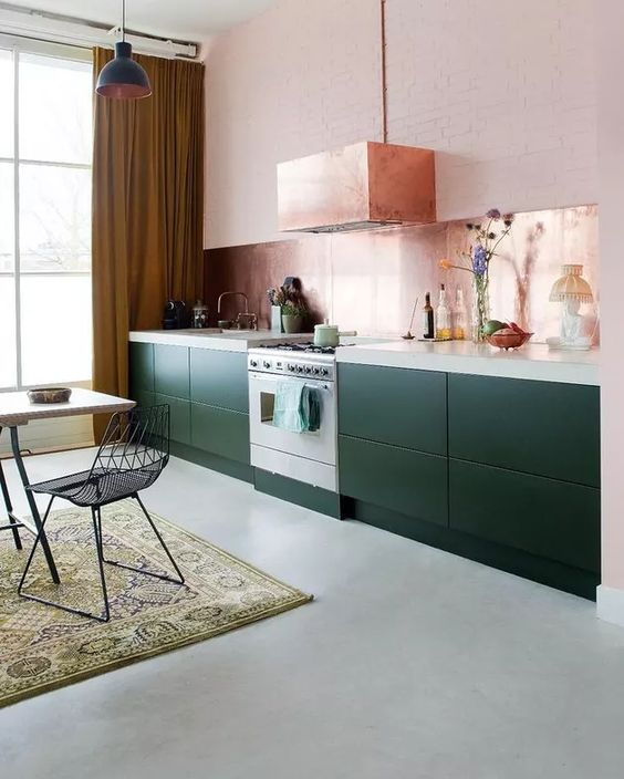 a dark green kitchen with only lower cabinets, a copper backsplash and a matching hood plus some blooms