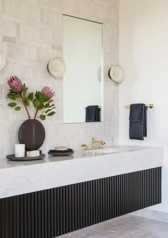 a chic bathroom with neutral tiles, a black fluted built-in vanity with a stone slab and gold fixtures