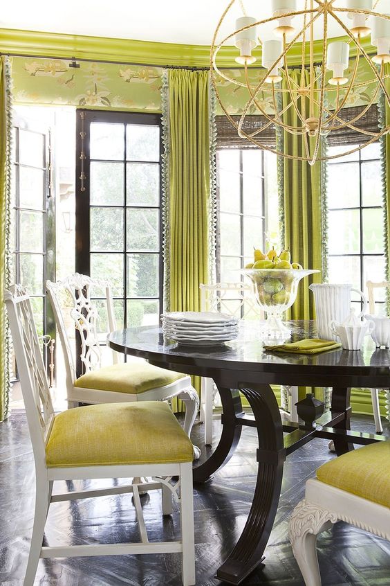 a bold eclectic dining room with chartreuse printed wallsa dn curtains, a dark table and yellow chairs plus a statement chandelier