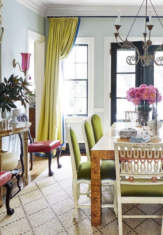 an exquisite dining room with a table, green chairs, chartreuse curtains, a printed rug, red chairs and some plants