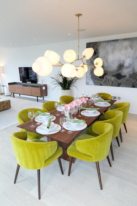 a modern dining room with a stained table, chartreuse chairs, a bubble chandelier and some art