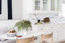 44 a chic white kitchen with a comfy dining nook, a banquette seating, wooden chairs and an oval table