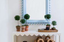 46 a pretty white scallop console table with potted plants, a basket storage unit, a vase and a mirror