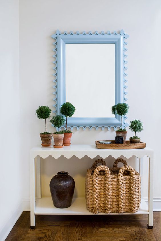 a pretty white scallop console table with potted plants, a basket storage unit, a vase and a mirror