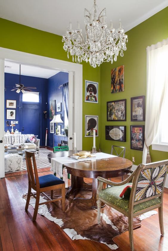 an eclectic dining room with chartreuse walls, a stained table, mismatching chairs, a crystal chandelier and a corner gallery wall