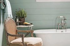 48 a mint green cottage bathroom with a vintage bathtub, a neutral antique chair, a side table with decor
