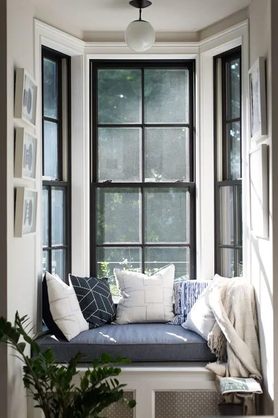 A double height bow window with a small windowsill and a built in seat with a cushions and pillows is a lovely nook to spend time