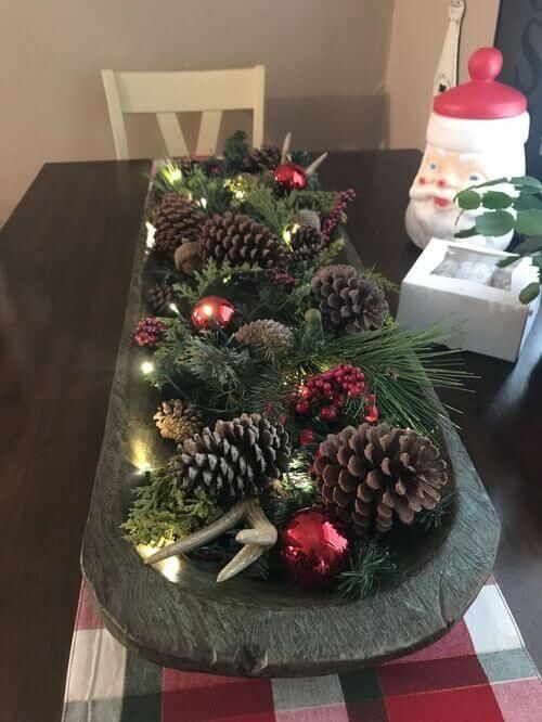 a Christmas arrangement of a dough bowl with evergreens, pinecones, ornaments, berries and lights