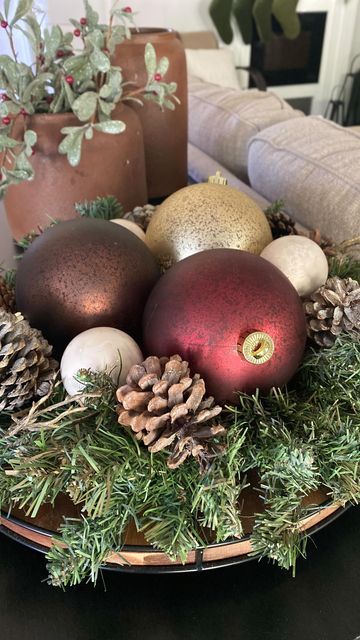 a Christmas arrangement of a wooden bowl with evergreens, brown, red and gold ornaments is cool