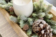 a Christmas centerpiece of a dough bowl with evergreens and pinecones plus a candle in a glass