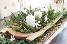 a Christmas centerpiece of a dough bowl with evergreens, pinecones, snowflakes and pillar candles is chic