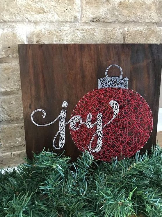 a Christmas string art piece showing an ornament and calligraphy, done with red and white yarn