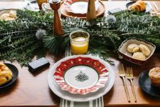 a Christmas tablescape with greenery and allium, candles, printed plates, bowls and plates with various sweets
