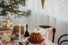 a Christmas tea party table with evergreens, a bundt cake, candles and sweets and printed textiles plus cones over the table