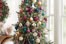 a Christmas tree decorated with colorful ornaments, purple, navy and teal ones, plus beaded garlands