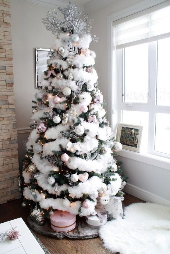 a Christmas tree with white faux fur, lights, white and pink ornaments, silver touches and chic round gift boxes under it