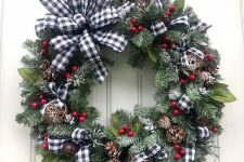 a Christmas wreath of evergreens, foliage, yarn balls, bells, pinecones and red berries plus a plaid bow on top