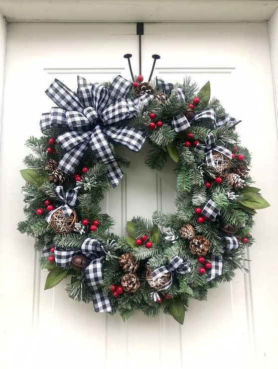 a Christmas wreath of evergreens, foliage, yarn balls, bells, pinecones and red berries plus a plaid bow on top