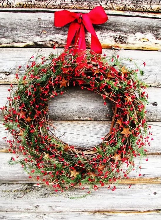 a Christmas wreath of greenery, vines and red berries plus a red ribbon bow for a rustic and cozy feel