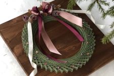 a Christmassy string art showing off a wreath, decorated with pinecones and ribbons, is a cool and catchy idea