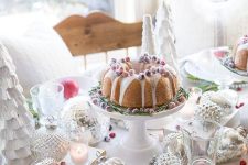 a beautiful Christmas table setting with a faux tree, large ornaments, white porcelain and red textiles, a bundt cake
