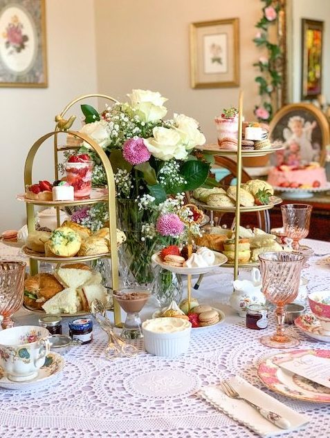 a beautiful Christmas tea party table with a doily tablecloth, floral porcelain, pink and white blooms, tiered stands with sweets and macarons