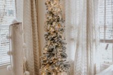 a beautiful flocked skinny Christmas tree with a bow and ribbons and lights plus a blanket wrap